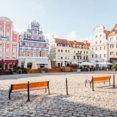 Kolorowy rynek miejski z kamienną nawierzchnią, ławkami i zabytkowymi kamienicami.