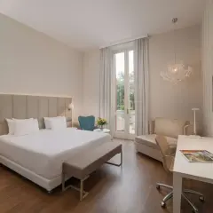 Elegancki pokój hotelowy z dużym łóżkiem, biurkiem i fotelem. Widok na taras z zielenią. Idealne miejsce na wypoczynek w kurorcie na riwierze francuskiej.