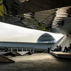 Nowoczesna architektura i nietypowe atrakcje Katowice: ludzie odpoczywają pod futurystycznym zadaszeniem, w tle kopuła Muzeum Śląskiego.