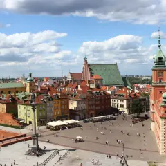 Widok na Zamek Królewski i Kolumnę Zygmunta III Wazy na placu w warszawskiej starówce. Tłumy spacerują po bruku, a słońce przebija się przez chmury.