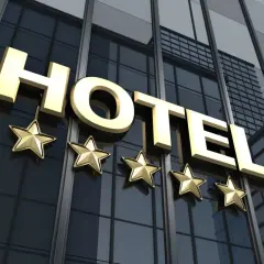 Złoty napis HOTEL i pięć gwiazdek na tle nowoczesnego budynku hotelowego.