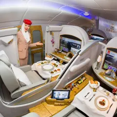 Stewardessa Emirates wita pasażera w luksusowej kabinie, oferując posiłek i rozrywkę. To szczyt komfortu podróży, oferowany przez jedne z największych linii lotniczych.