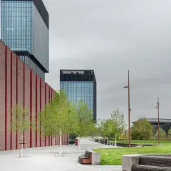 Nowoczesna architektura i zieleń tworzą ciekawe miejsca do 100 km od Katowic. Park z ławkami i drzewami przed szklanymi wieżowcami.
