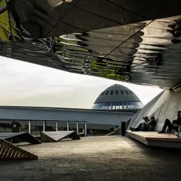 Nowoczesna architektura i nietypowe atrakcje Katowice: ludzie odpoczywają pod futurystycznym zadaszeniem, w tle kopuła Muzeum Śląskiego.