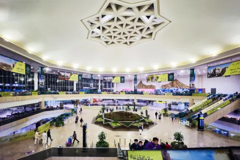 Wnętrze lotniska, które może być największym lotniskiem na świecie, z wielopoziomowymi galeriami, schodami ruchomymi i centralną zieloną przestrzenią.
