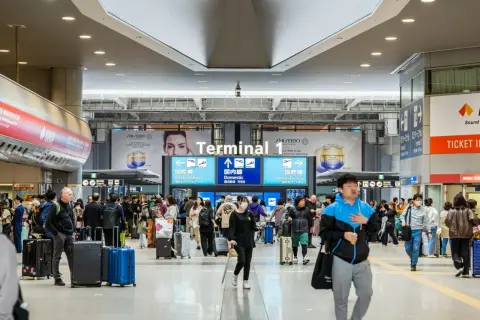 Tłum ludzi z walizkami w Terminalu 1 lotniska. Czy do Japonii potrzebna jest wiza? Wszyscy zmierzają do bramek, niektórzy w maseczkach.