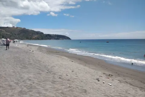 Plaża na wyspie Dominika z ciemnym piaskiem, turkusową wodą i zielonymi wzgórzami w tle.