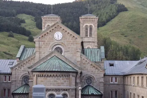 Bazylika Matki Bożej z La Salette, kamienna budowla z wieżami i zegarem, wznosi się na tle zielonych górskich zboczy.