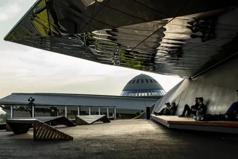 Nowoczesna architektura i nietypowe atrakcje Katowice: ludzie odpoczywają pod futurystycznym zadaszeniem, w tle kopuła Muzeum Śląskiego.