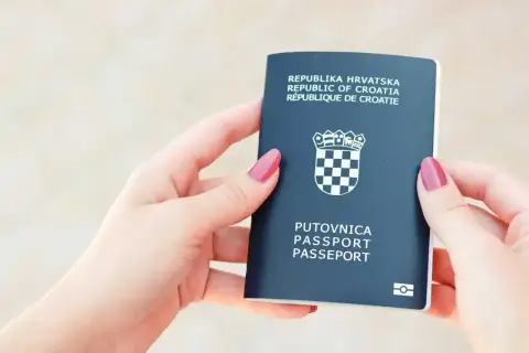 Dwie dłonie trzymają ciemnogranatowy paszport Republiki Chorwacji. Czy do Chorwacji potrzebny jest paszport? Tak, ten dokument jest niezbędny.