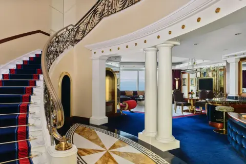 Luksusowe wnętrze z marmurowymi schodami, złotymi zdobieniami i niebieskim dywanem. To widok, który może towarzyszyć pobytowi w Burj Al Arab, gdzie burj al arab cena za noc odzwierciedla tę elegancję.