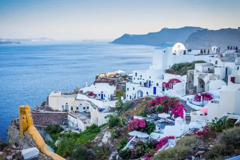 Widok na białe domy Santorini z niebieskimi drzwiami i oknami, kwitnące bugenwille. Czy do Grecji potrzebny jest paszport? Tak, jeśli nie jesteś obywatelem UE.