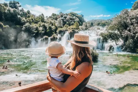 Mama z dzieckiem podziwia piękne krka wodospady. Woda w rzece jest krystalicznie czysta, a wokół bujna zieleń.
