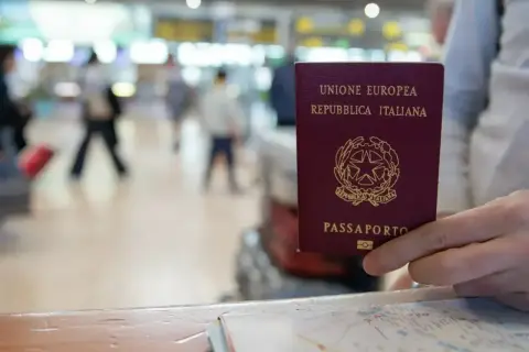 Włoski paszport w dłoni. Czy do Serbii potrzebny jest paszport? W tle lotnisko.