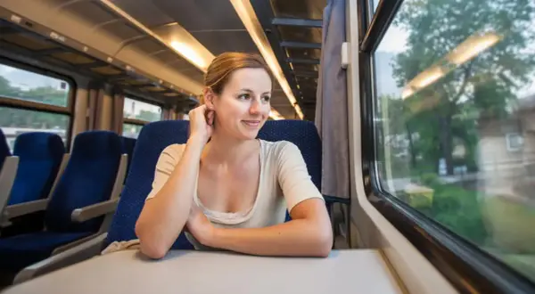 Uśmiechnięta kobieta w pociągu, marząca o wycieczkach pociągiem po Europie z Polski.