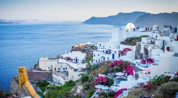 Widok na białe domy Santorini z niebieskimi drzwiami i oknami, kwitnące bugenwille. Czy do Grecji potrzebny jest paszport? Tak, jeśli nie jesteś obywatelem UE.