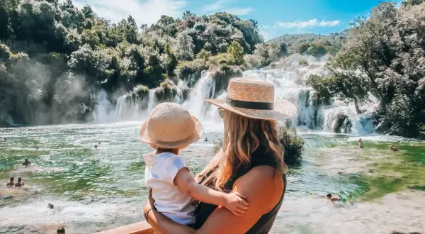 Mama z dzieckiem podziwia piękne krka wodospady. Woda w rzece jest krystalicznie czysta, a wokół bujna zieleń.