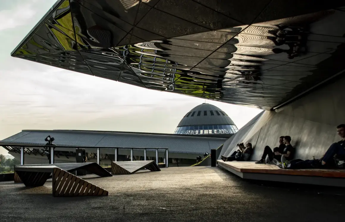 Nowoczesna architektura i nietypowe atrakcje Katowice: ludzie odpoczywają pod futurystycznym zadaszeniem, w tle kopuła Muzeum Śląskiego.