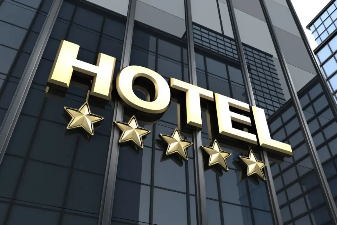 Złoty napis HOTEL i pięć gwiazdek na tle nowoczesnego budynku hotelowego.