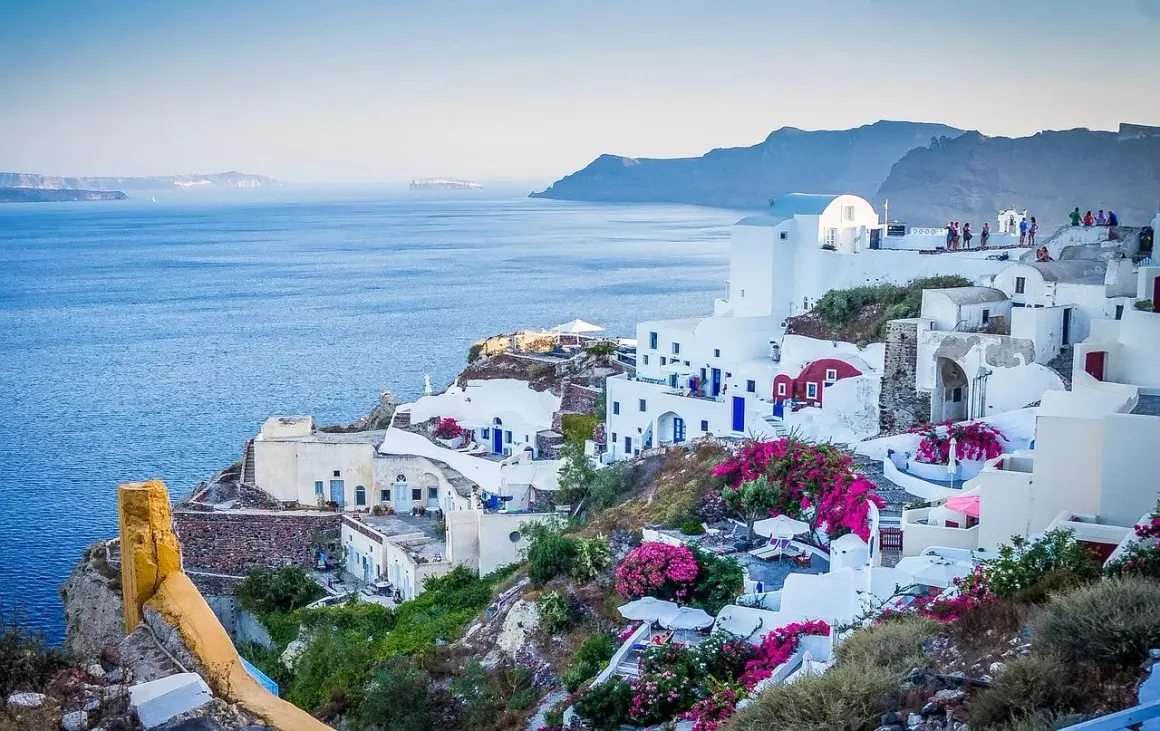 Widok na białe domy Santorini z niebieskimi drzwiami i oknami, kwitnące bugenwille. Czy do Grecji potrzebny jest paszport? Tak, jeśli nie jesteś obywatelem UE.