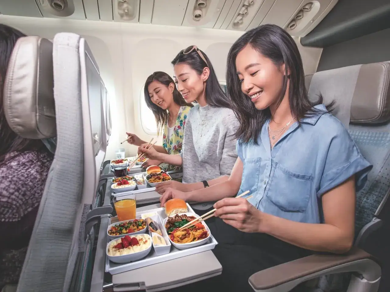 Uśmiechnięte pasażerki cieszą się posiłkiem w klasie ekonomicznej Emirates. Smaczne jedzenie i komfort podróży.