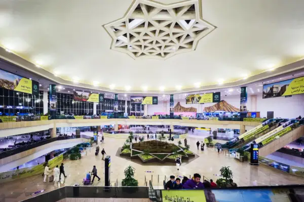 Wnętrze lotniska, które może być największym lotniskiem na świecie, z wielopoziomowymi galeriami, schodami ruchomymi i centralną zieloną przestrzenią.