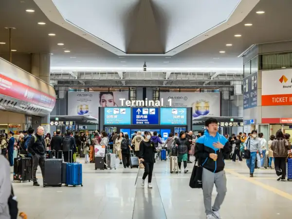 Tłum ludzi z walizkami w Terminalu 1 lotniska. Czy do Japonii potrzebna jest wiza? Wszyscy zmierzają do bramek, niektórzy w maseczkach.