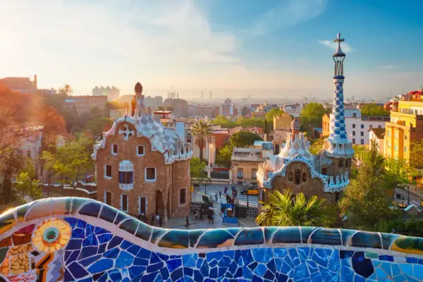 Kolorowa mozaika Parku Güell wita na wspaniałej **barcelona wycieczka**. Dwa bajkowe domki i wieża z krzyżem w tle.