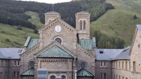 Bazylika Matki Bożej z La Salette, kamienna budowla z wieżami i zegarem, wznosi się na tle zielonych górskich zboczy.