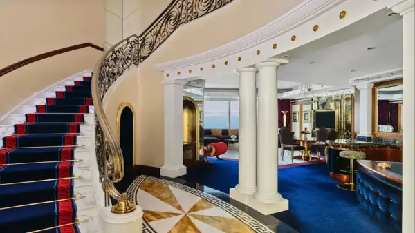 Luksusowe wnętrze z marmurowymi schodami, złotymi zdobieniami i niebieskim dywanem. To widok, który może towarzyszyć pobytowi w Burj Al Arab, gdzie burj al arab cena za noc odzwierciedla tę elegancję.