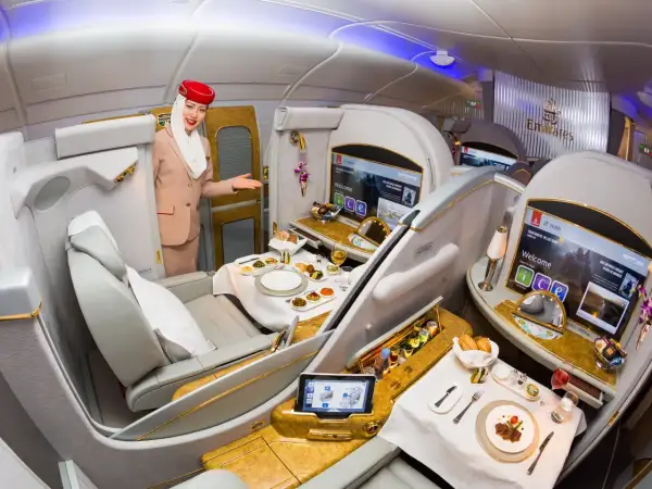 Stewardessa Emirates wita pasażera w luksusowej kabinie, oferując posiłek i rozrywkę. To szczyt komfortu podróży, oferowany przez jedne z największych linii lotniczych.