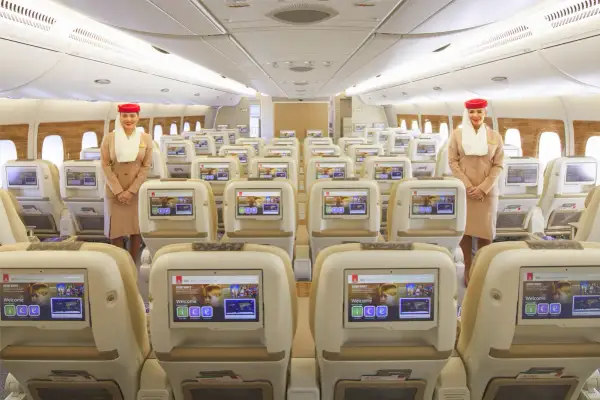 Uśmiechnięta stewardessa w klasie ekonomicznej Emirates. Rzędy wygodnych foteli z ekranami pokładowymi.