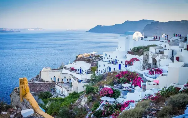 Widok na białe domy Santorini z niebieskimi drzwiami i oknami, kwitnące bugenwille. Czy do Grecji potrzebny jest paszport? Tak, jeśli nie jesteś obywatelem UE.