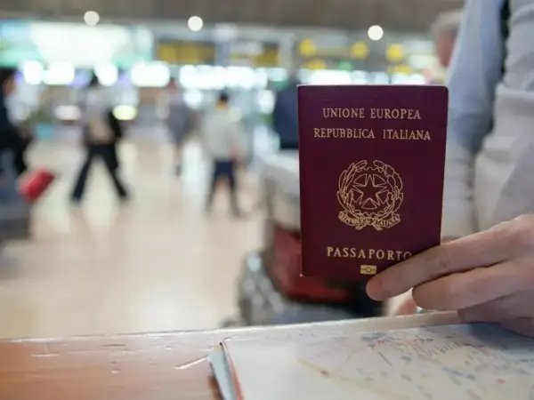 Włoski paszport w dłoni. Czy do Serbii potrzebny jest paszport? W tle lotnisko.